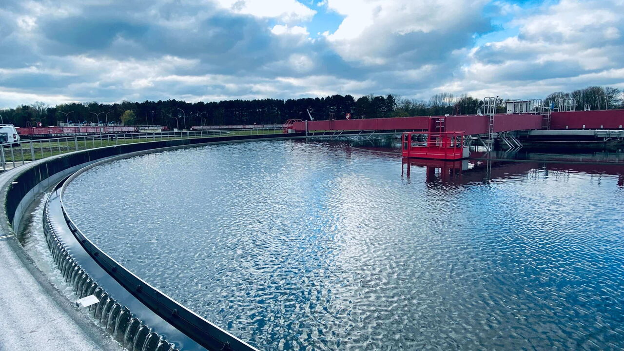 Nachklärbecken mit Ablaufrinne im Vordergrund, blauer Himmel mit Wolken.