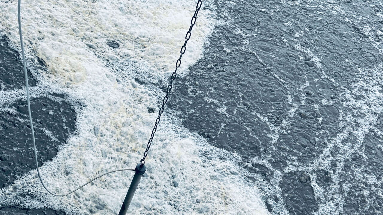 Messsonde, die über einer blubbernden Wasseroberfläche an einer Kette hängt.
